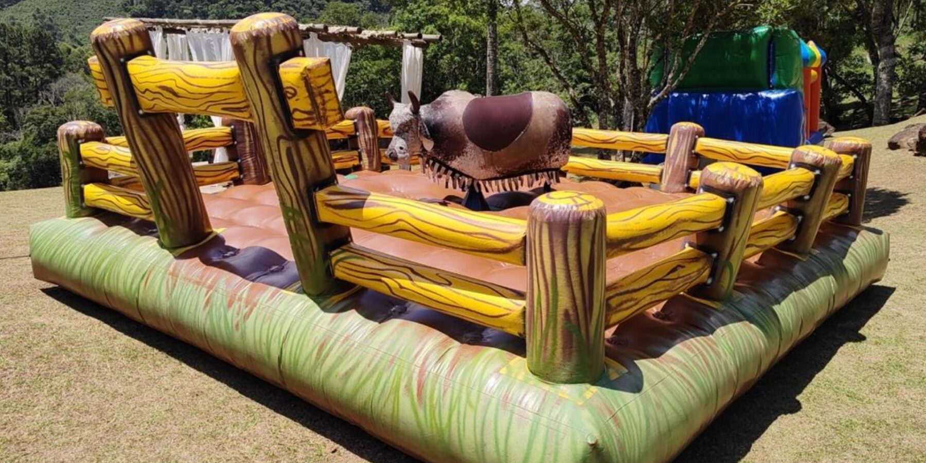 Touro mecânico da Castelinho Kids montado em área externa, com o colchão inflável temático de cerquinha em volta da base