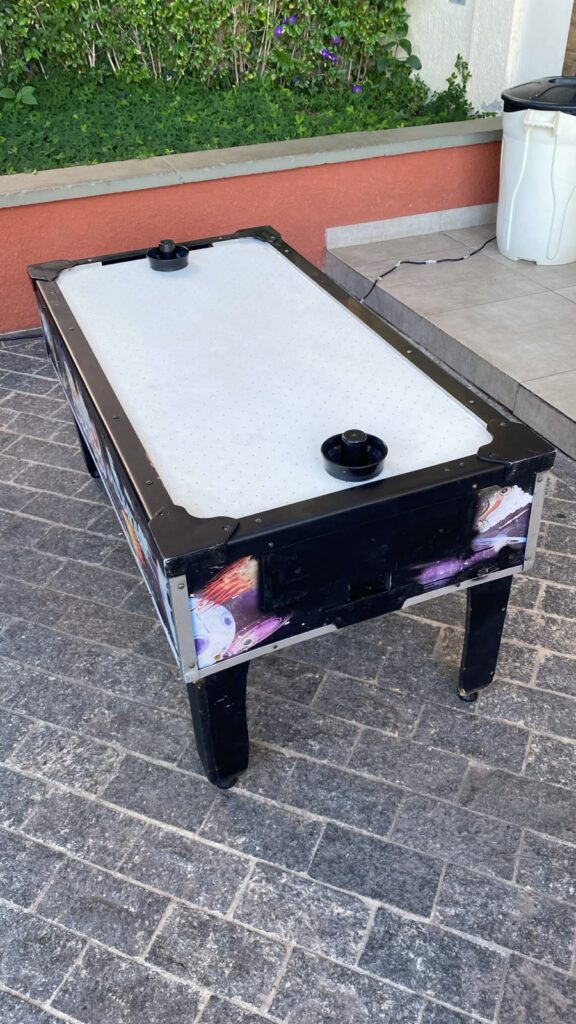 Mesa de air game com tampo branco e dois discos, montada na área externa de uma casa