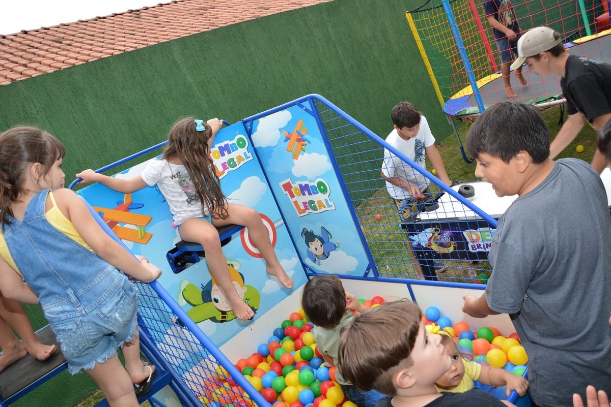 Crianças brincando juntas numa festa infantil, no Tombo Legal e na piscina de bolinhas, com adultos em volta