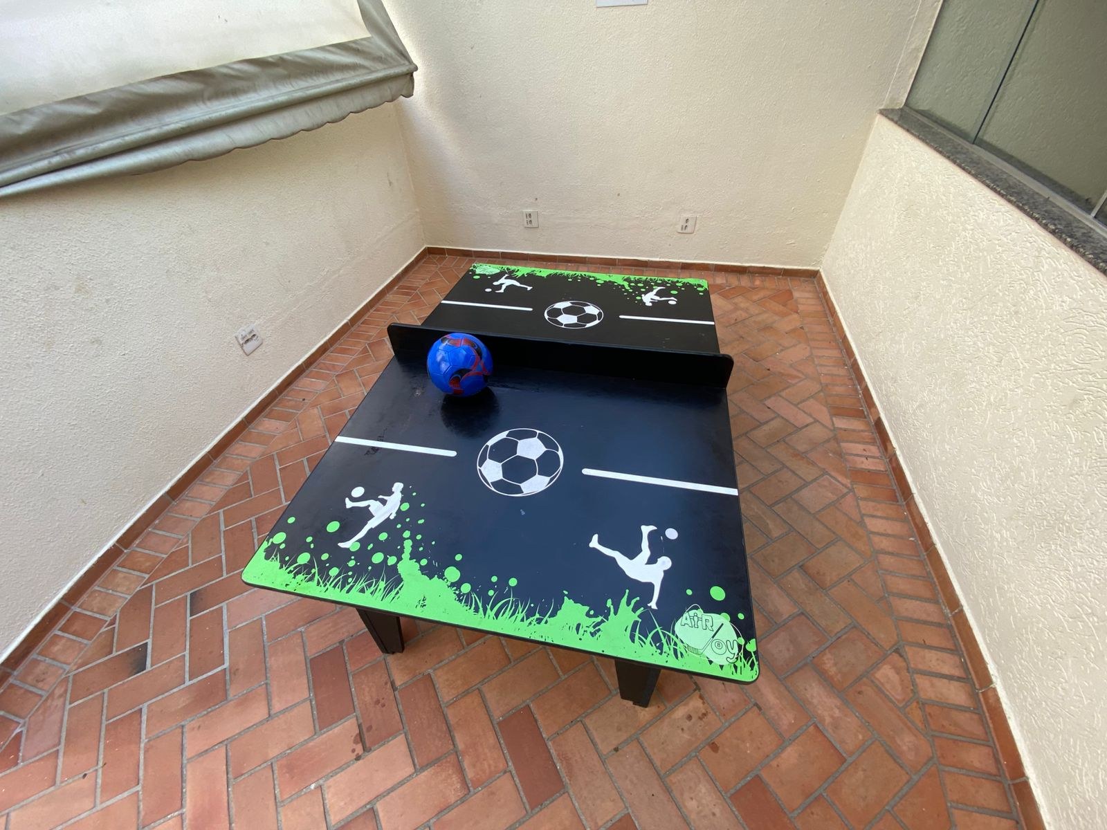 Quatro meninos jogando na mesa de ping pong e no pebolim montados lado a lado