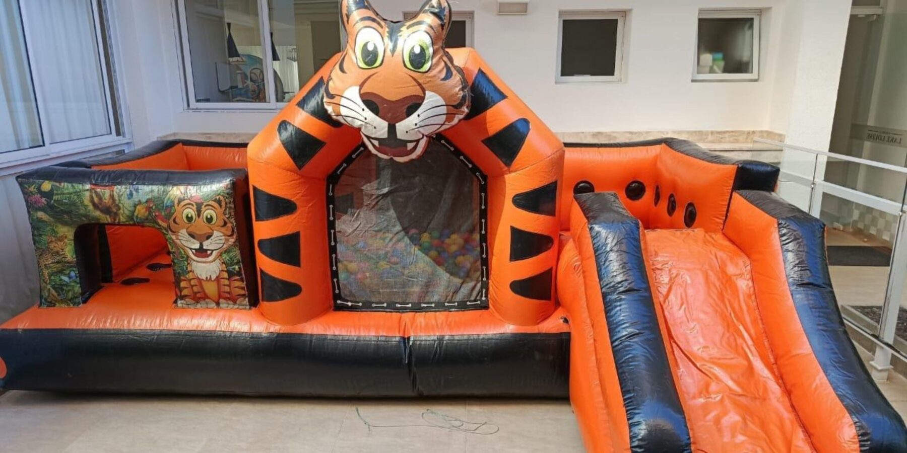 Brinquedo inflável multiatividade com tema de tigre, piscina de bolinhas e escorregador, montado em área externa