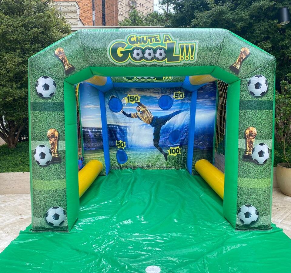 Chute a Gol inflável visto de frente, com a trave verde, os alvos de 50, 100 e 150 pontos no fundo e o tapete verde, montado em terraço de prédio, aluguel Castelinho Kids