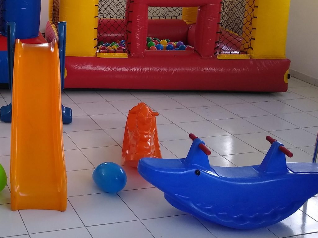 Kit Playground montado em salao de festa, com escorregador laranja, gangorra cavalinho laranja e gangorra azul de dois lugares no piso branco, aluguel Castelinho Kids