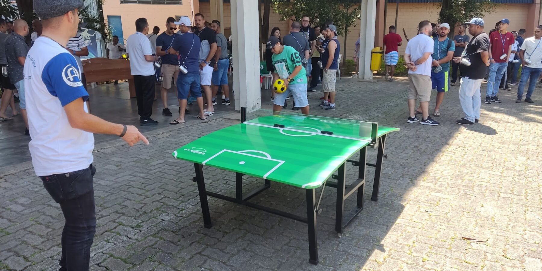 Futmesa montada em área externa durante a confraternização de uma empresa, com convidados jogando e conversando em volta