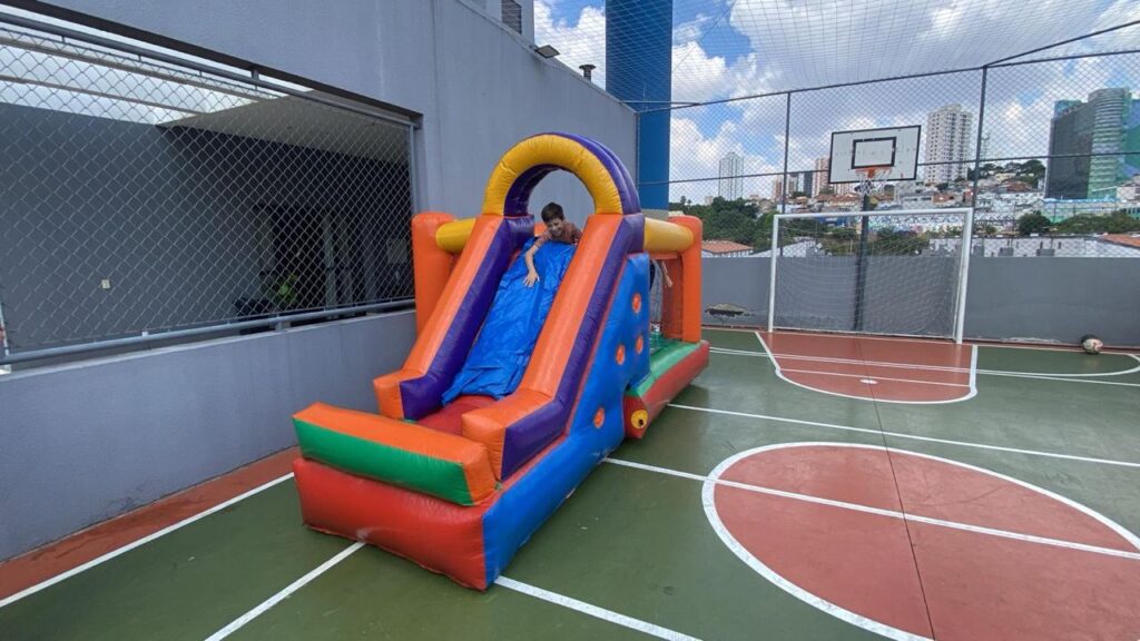 Tobogã inflável montado na quadra de um condomínio, com criança descendo